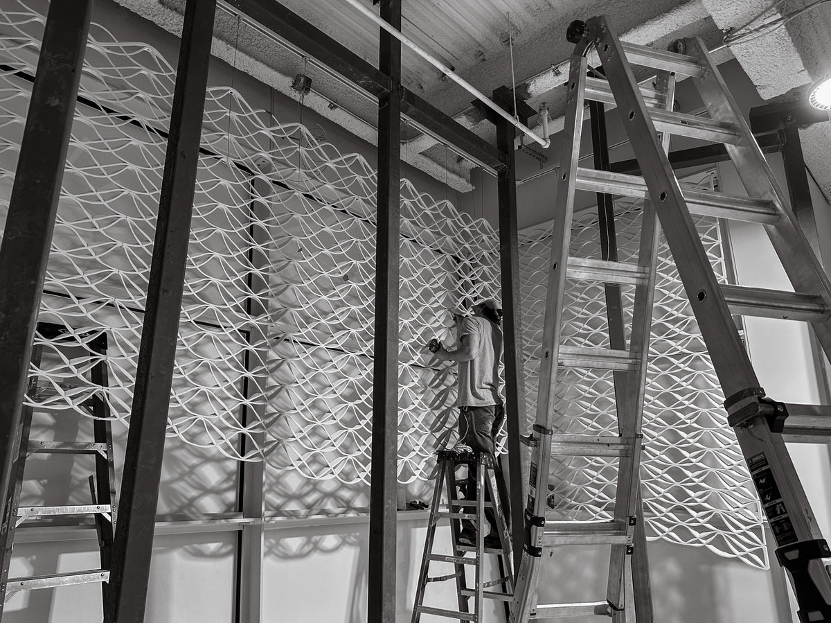 Installer aligning printed mesh panels inside a lululemon Prudential Center window bay, framed by ladders and structural steel in Boston.