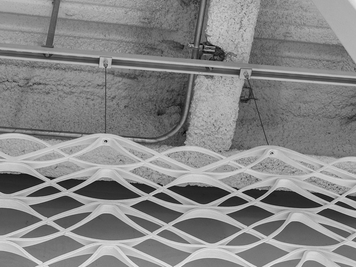 Close view of Unistrut, aircraft cable, and attachment points suspending printed mesh panels at lululemon Prudential Center in Boston.