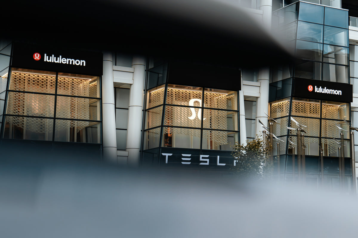 Three illuminated lululemon window bays at Prudential Center seen through a blurred foreground element, emphasizing depth across the Boston storefront.