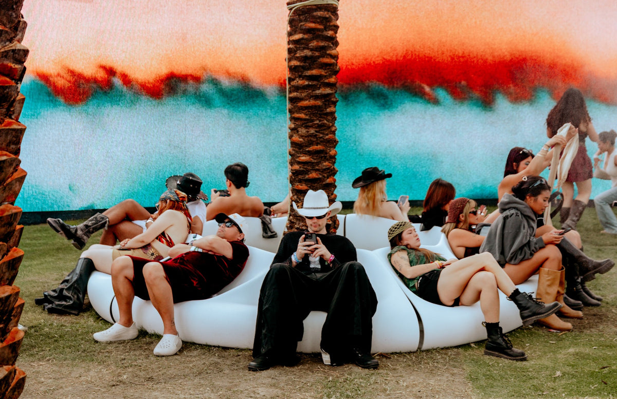 Festival guests gathered on white sculptural Decibel seating around a palm tree at SKYLRK’s OASIS at Coachella.