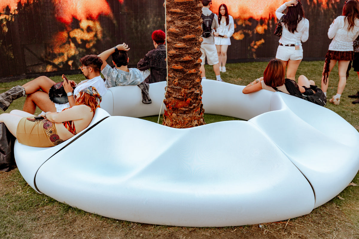 Curved white bench modules forming a seating ring around a palm tree at Coachella.