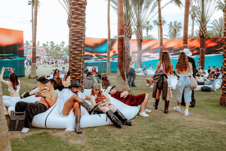 Wide view of guests and white modular seating among palm trees at SKYLRK’s Coachella installation.