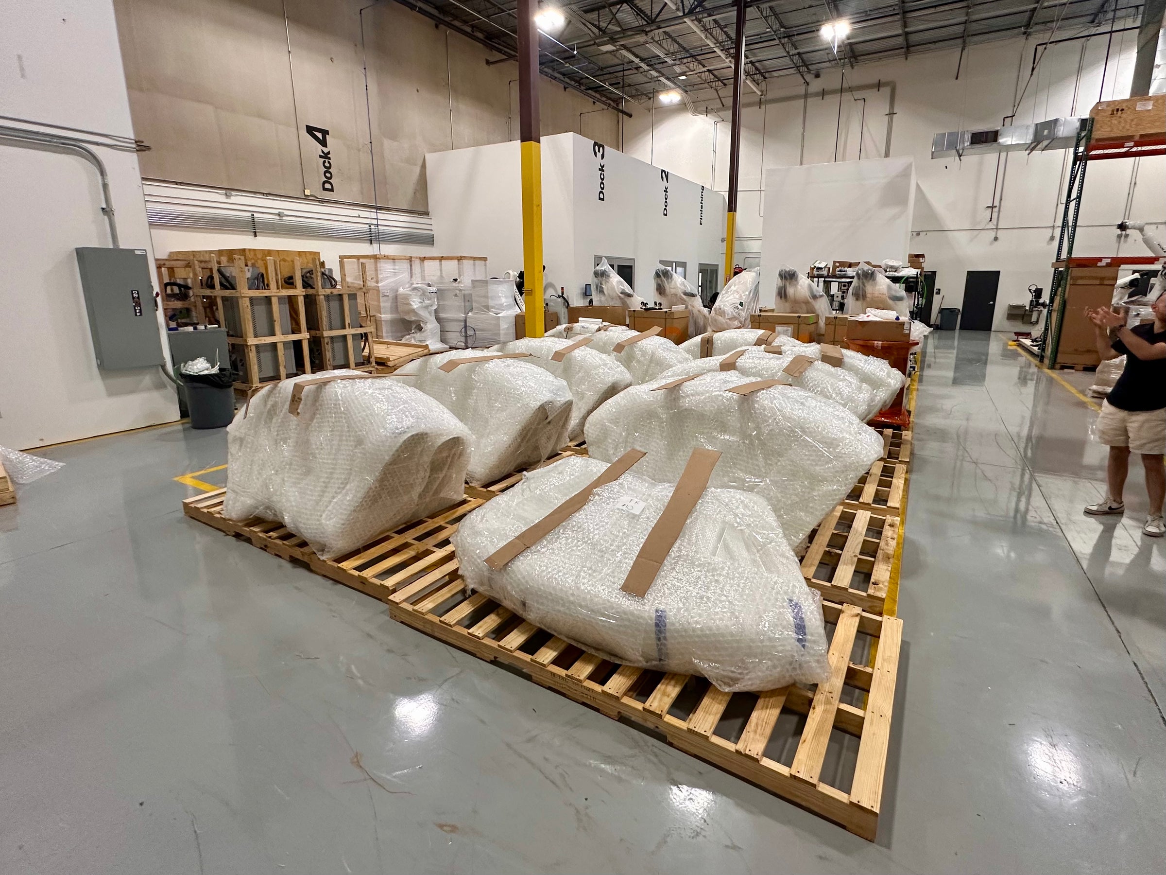 Wrapped seating components secured to wooden pallets in a fabrication workshop.