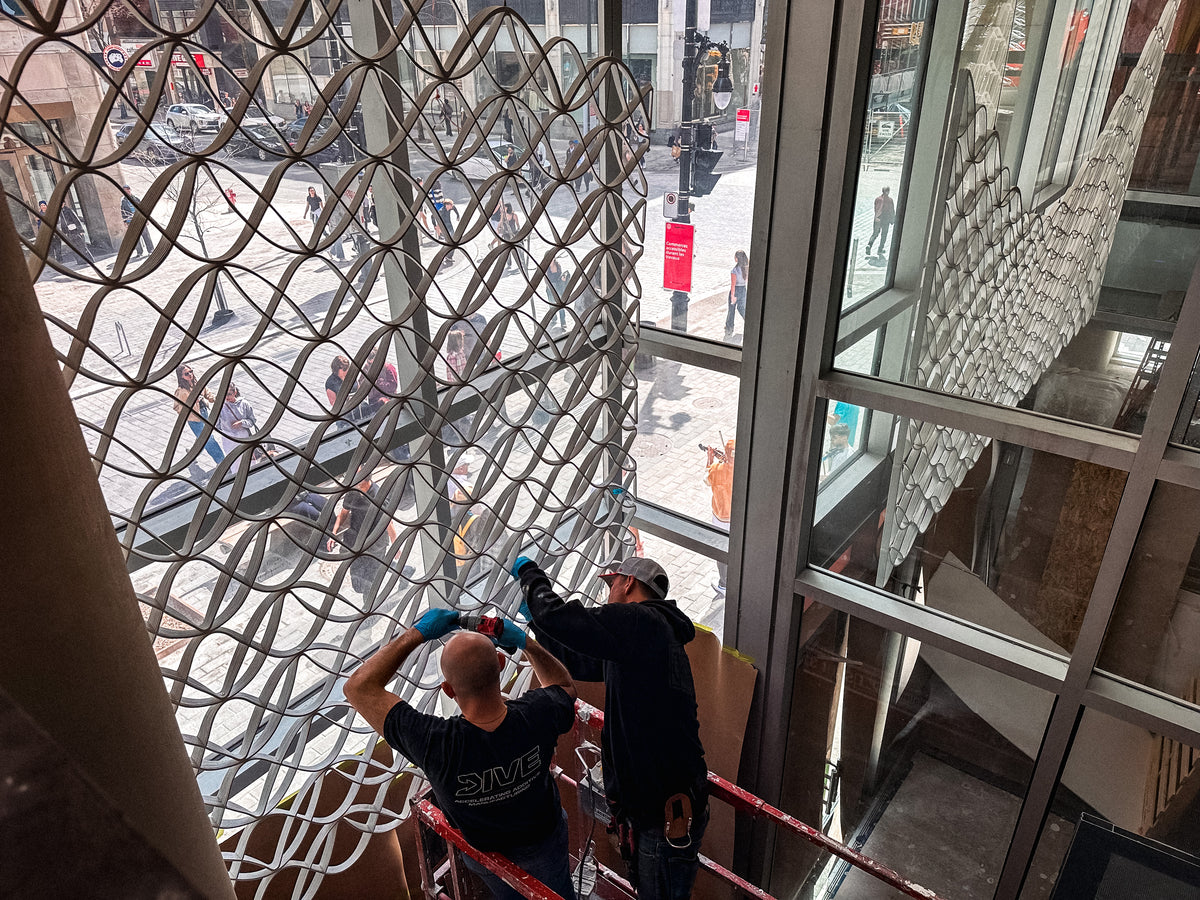 Installers positioning architectural mesh panels inside the Montréal storefront window.