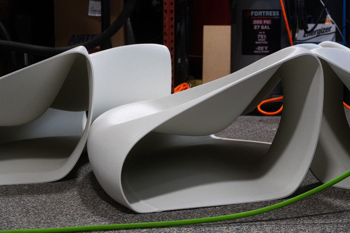White sculptural bench modules with open sides and continuous curved surfaces in the workshop.