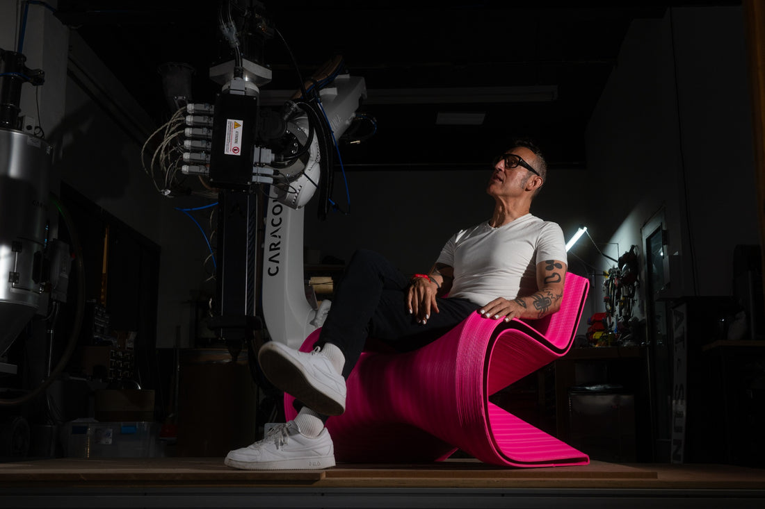 Designer seated in a sculptural pink 3D-printed chair beside Decibel’s robotic fabrication system in the New Jersey studio.