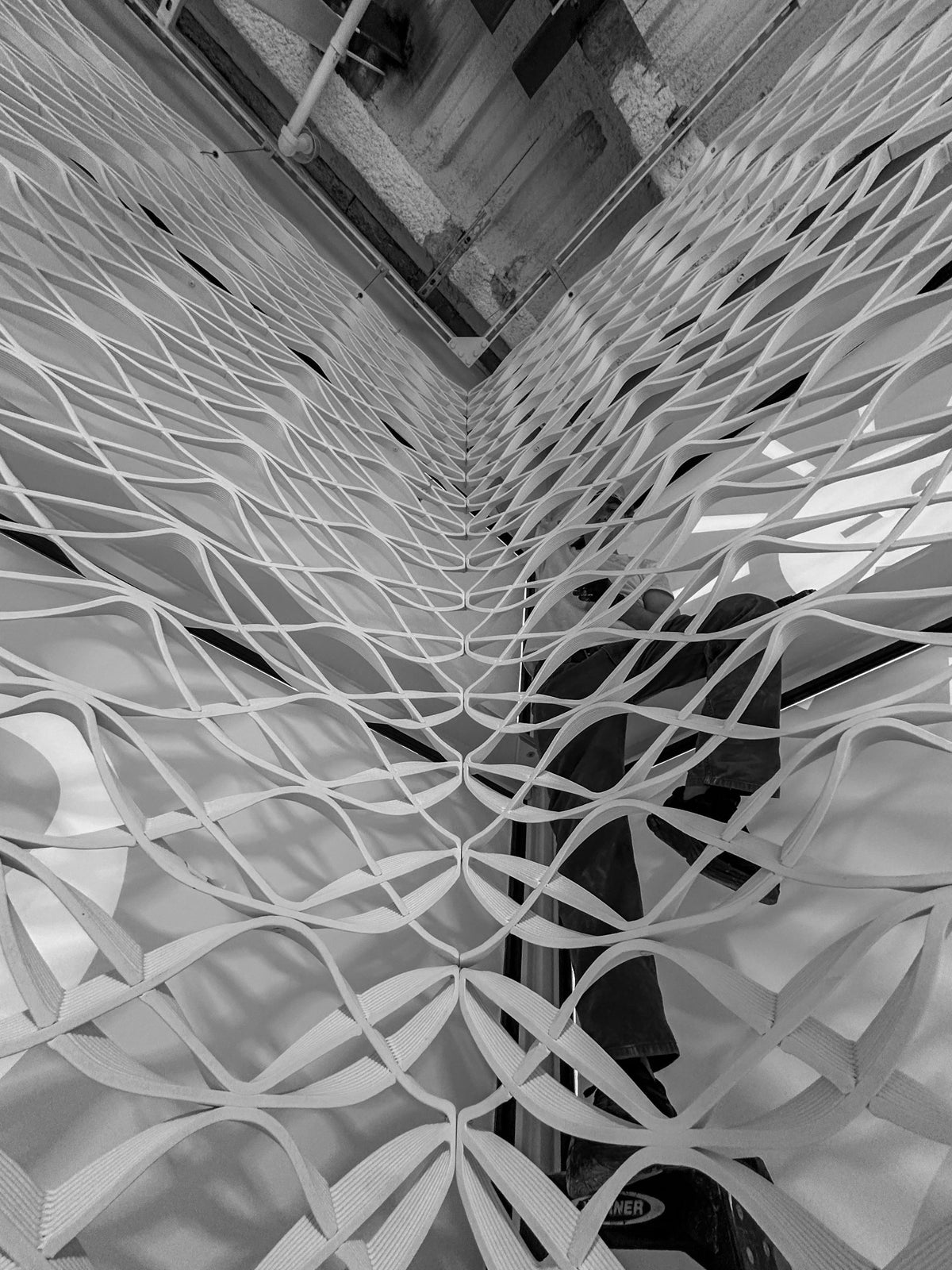 Black-and-white view into a corner where printed mesh panels meet during installation at lululemon Prudential Center in Boston.