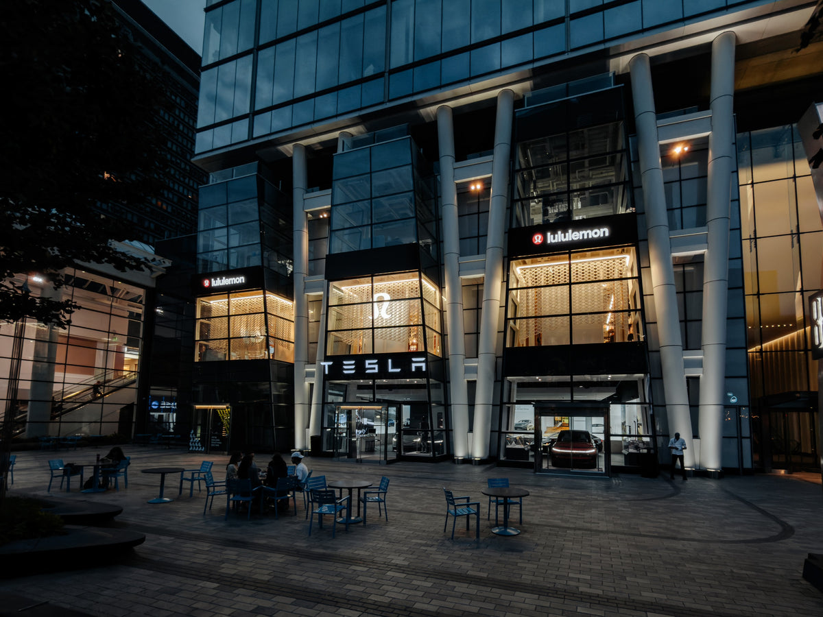 Wide dusk view of the three illuminated lululemon Prudential Center bays from the plaza, showing the mesh installation within the larger Boston facade.