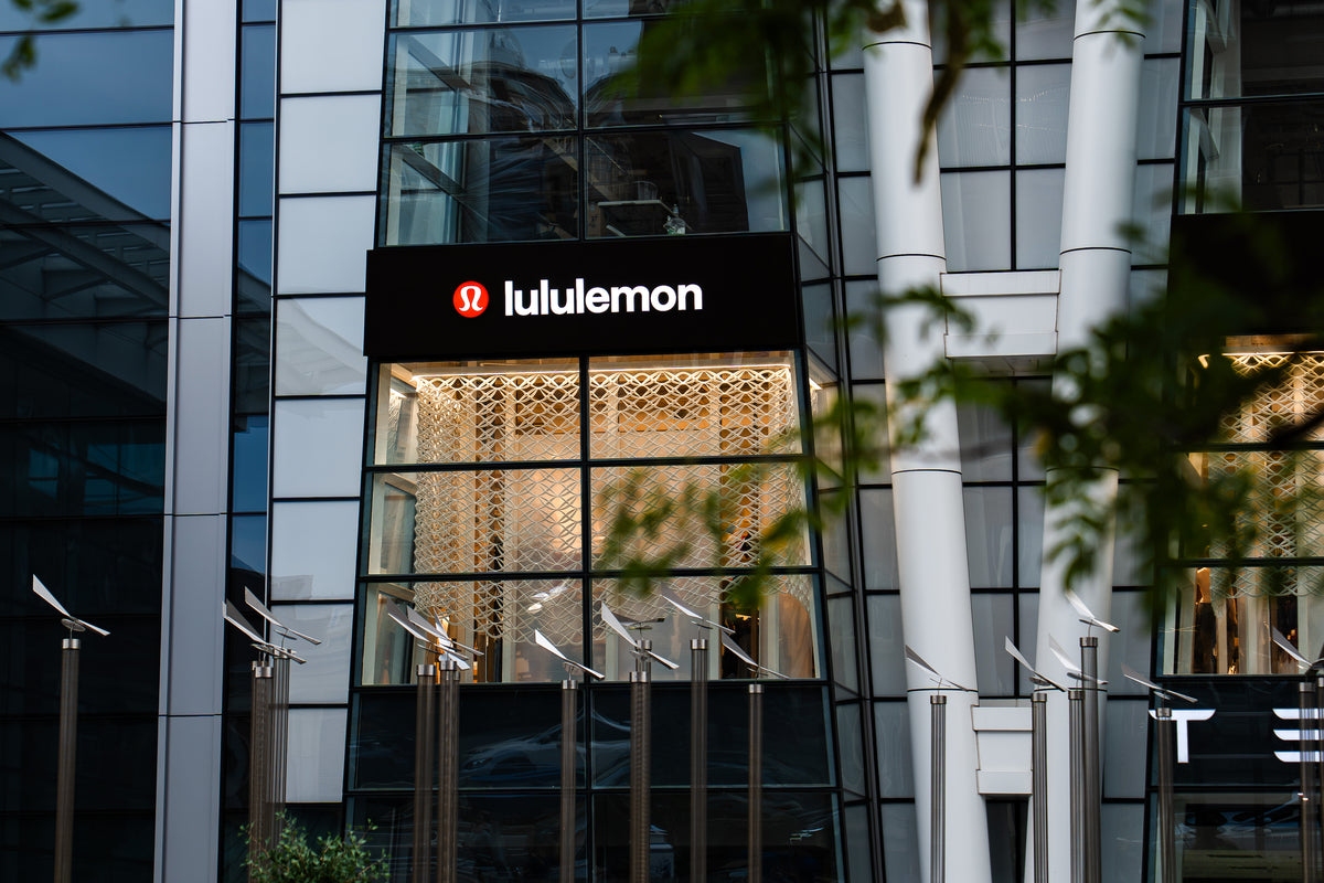 Tree-framed view of an illuminated lululemon Prudential Center bay showing the printed mesh installation behind the glazing.