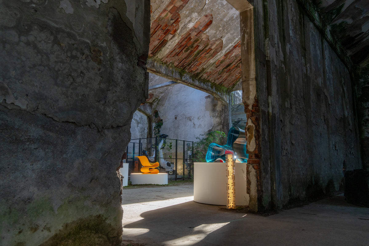 Colorful chairs displayed on white plinths inside the industrial setting of the PORTAL exhibition at Alcova.