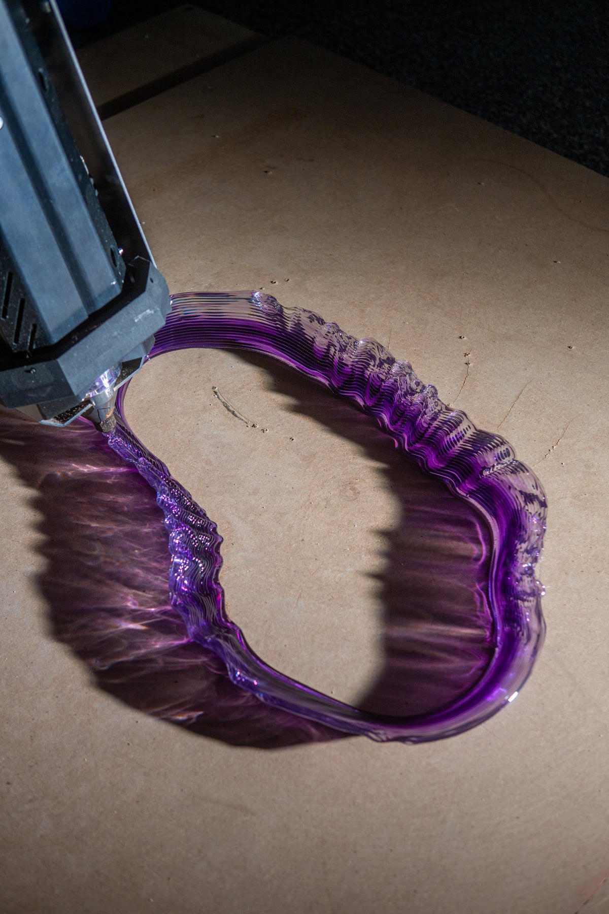 Purple curved component being produced beneath a robotic printing nozzle.