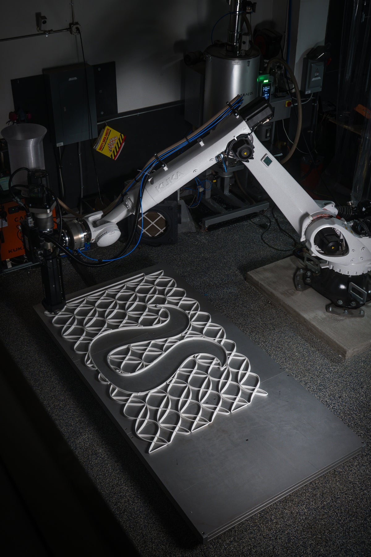 Robotic arm producing open-pattern architectural mesh panels on a fabrication table.