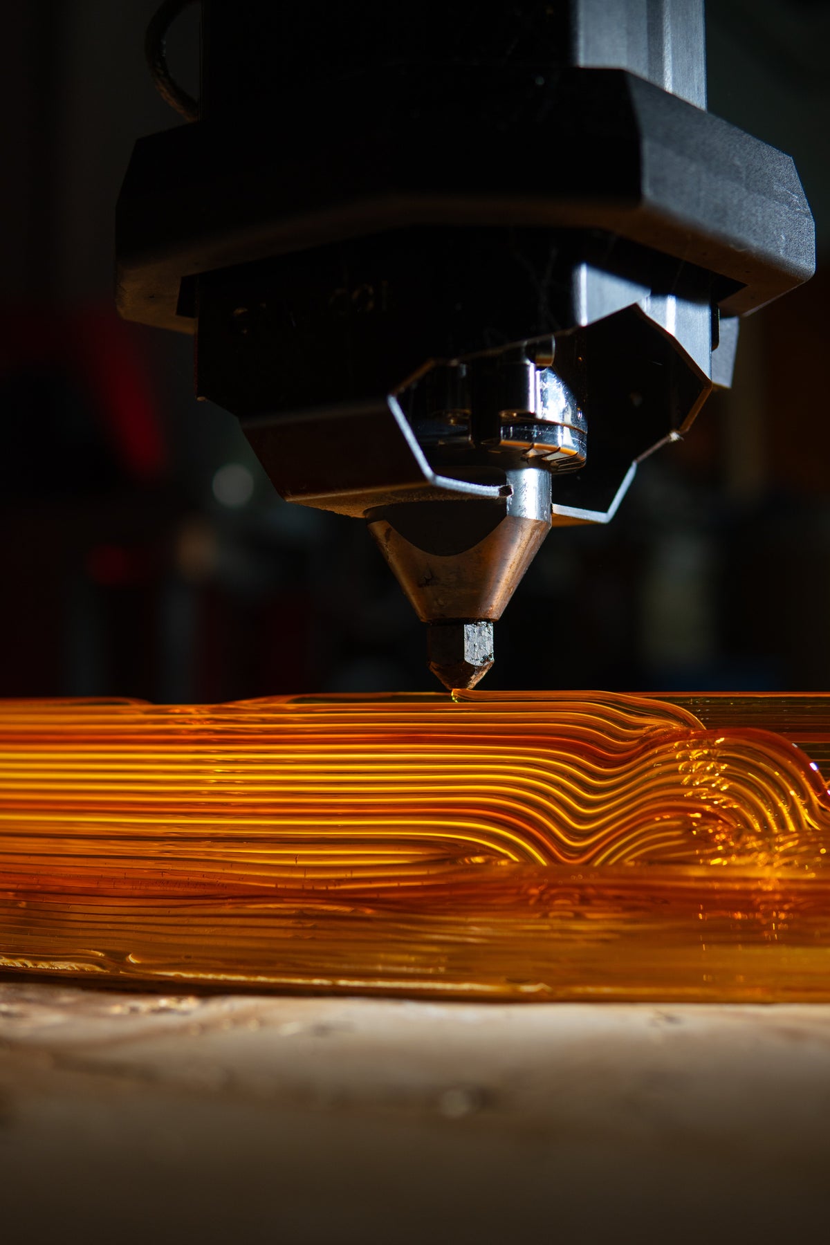 Robotic printing nozzle depositing layers onto an orange curved component.