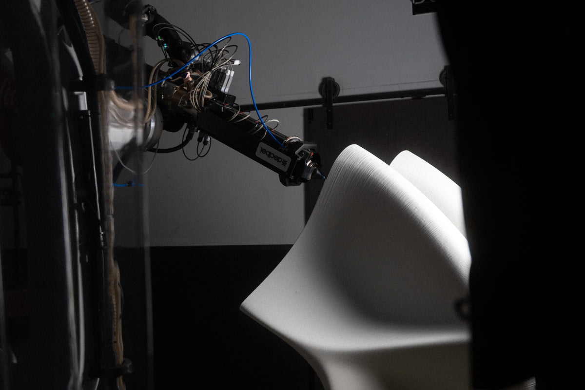 Close view of a robotic print head shaping the curved edge of a white SKYLRK bench during production at Decibel.