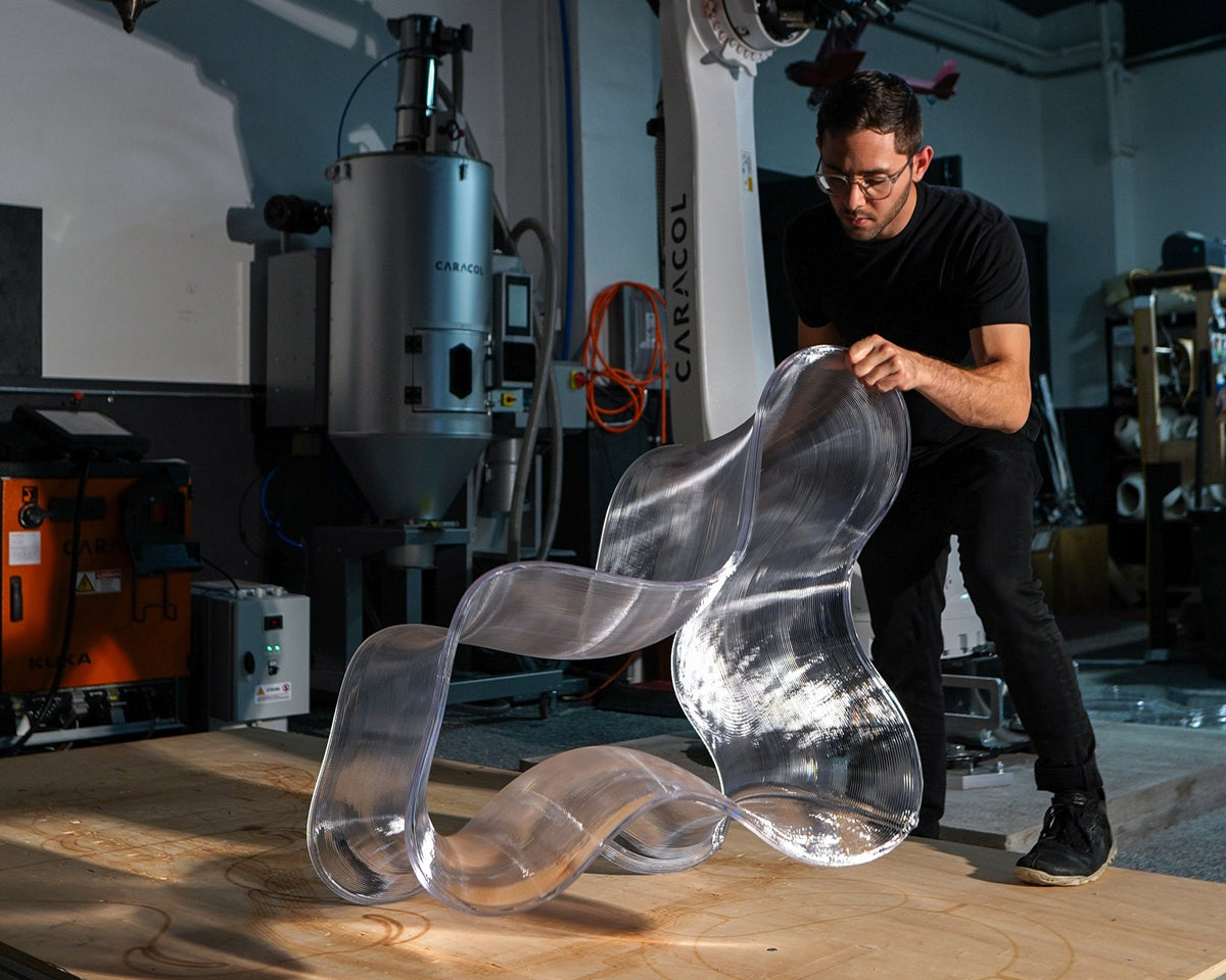 A designer examining a transparent sculptural chair in Decibel’s robotic fabrication workshop.