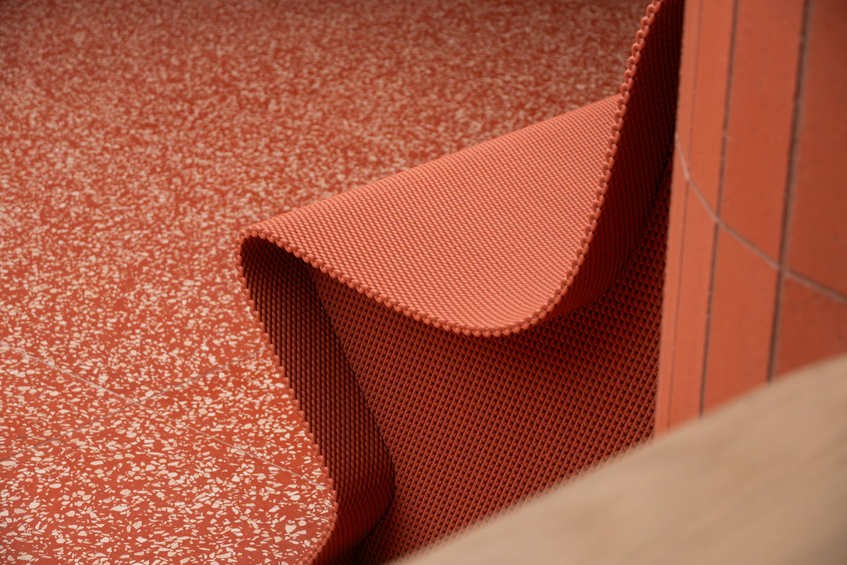 Overhead detail of a curved red bench edge against a speckled retail floor.