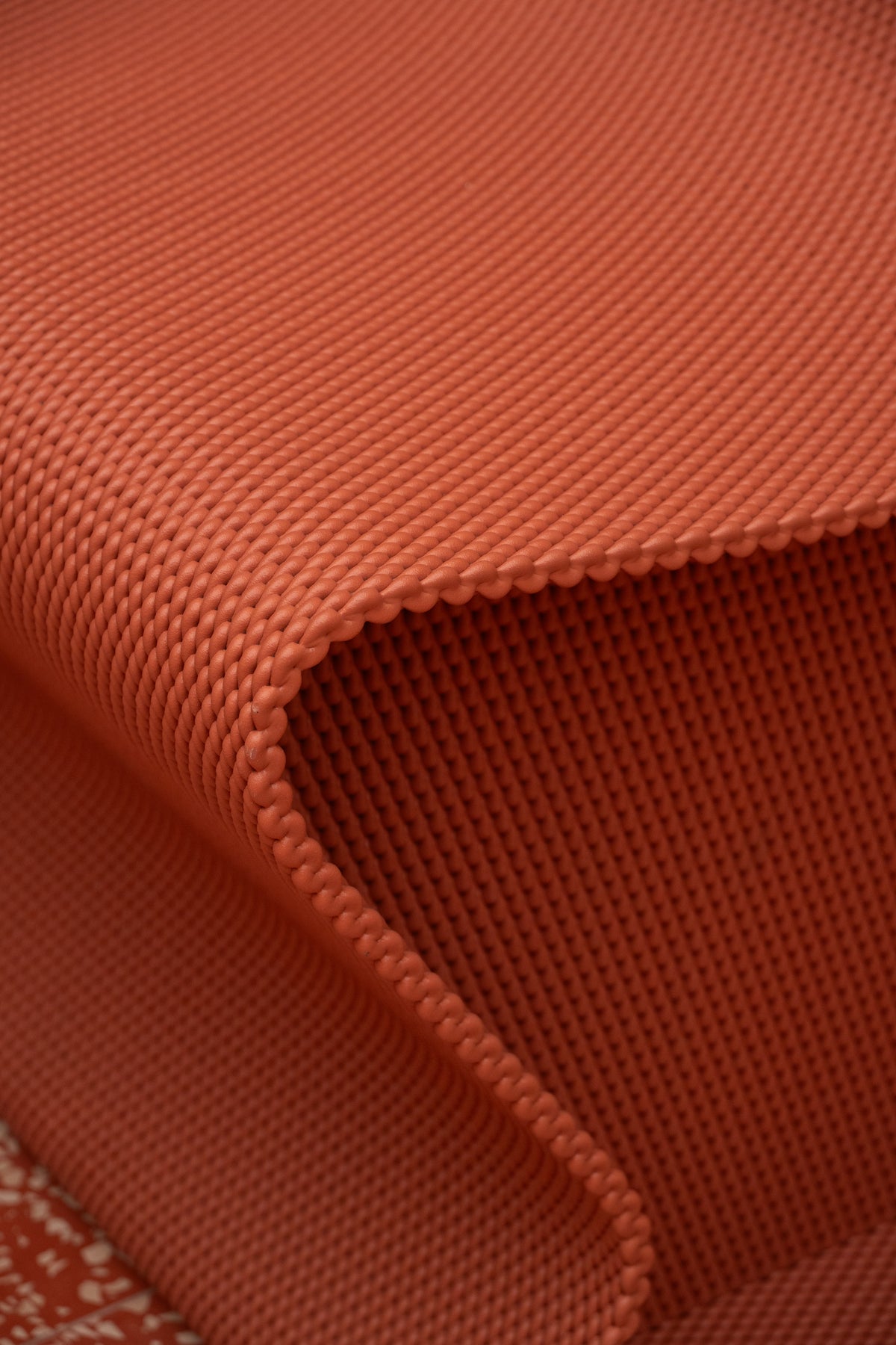 Close-up of the fine repeating surface pattern and curved edge of a red 3D-printed bench.