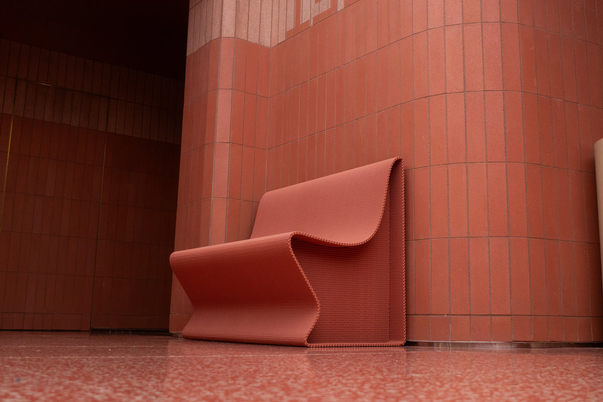 Side view of a red sculptural bench against matching tile at lululemon SoHo.