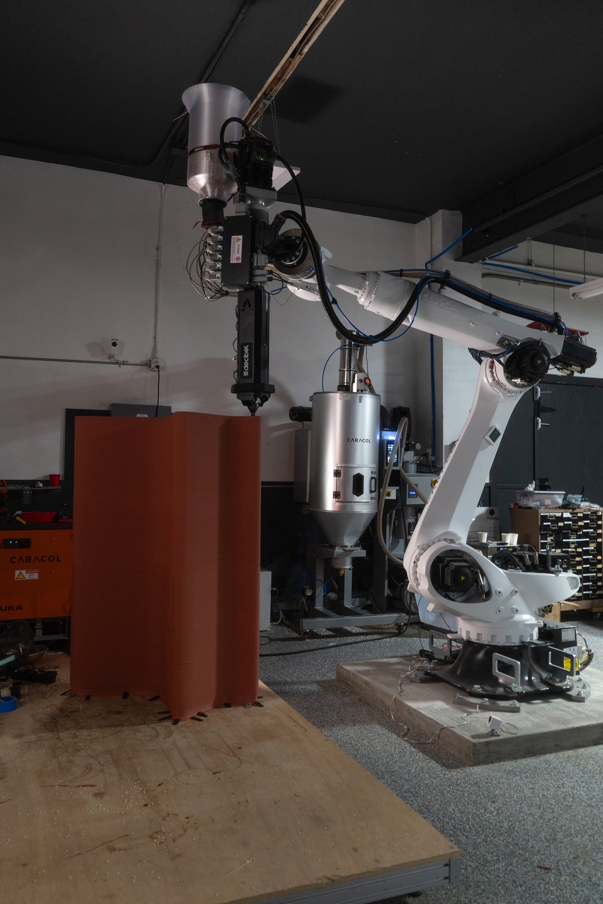 Robotic fabrication equipment beside a red printed bench component in Decibel’s workshop.