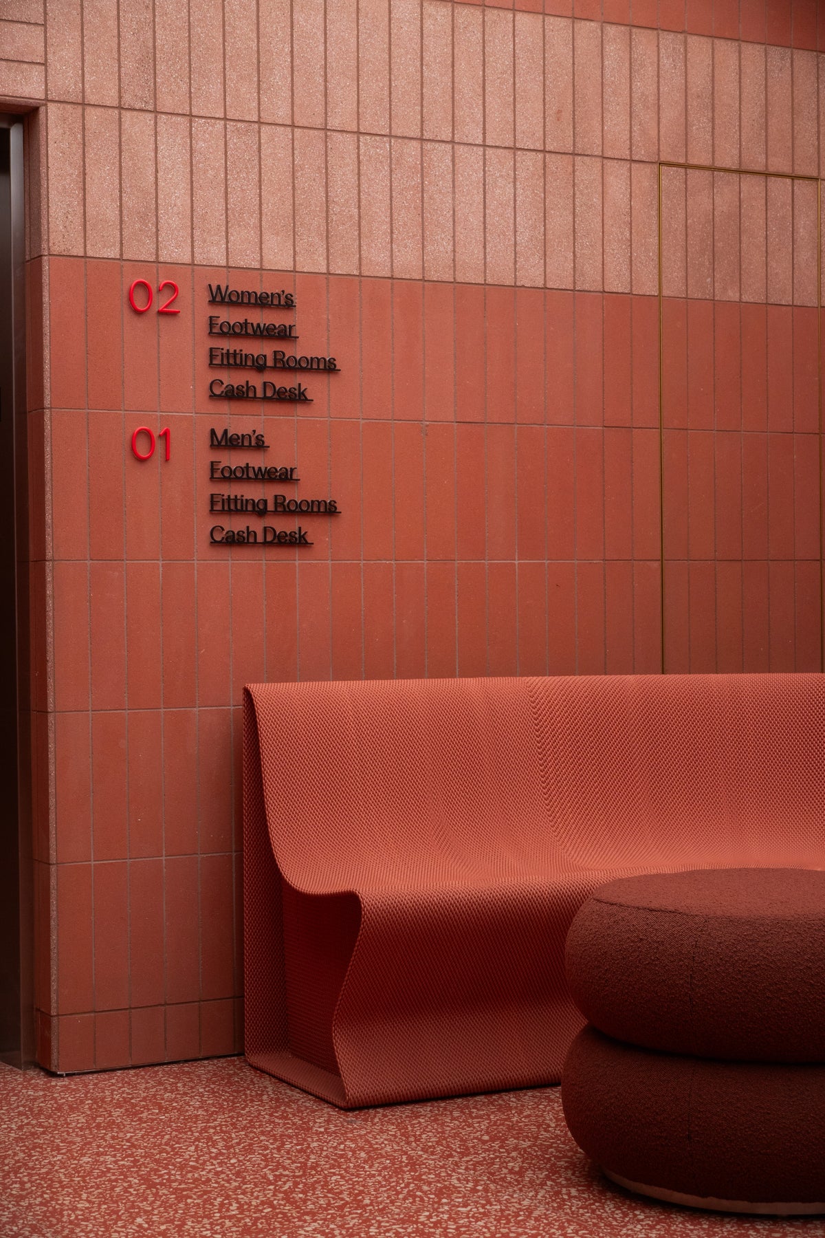 Custom red bench and round seat against the tiled wayfinding wall at lululemon SoHo.